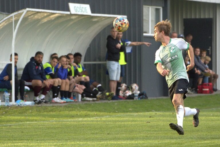 A Galicja Raciborowice player dominating the ball with the Krakow Dragoons FC bench in the background