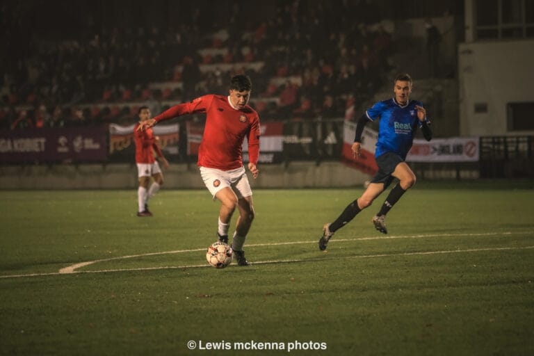 A FC United of Manchester player carrying the ball inside the Krakow Dragoons FC box, instants before scoring the first goal of the match