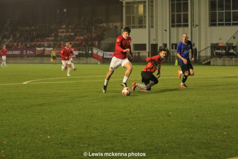 A FC United of Manchester player goes around goalkeeper Marcin Obyrtacz of Krakow Dragoons FC and prepares to hit the ball against the net