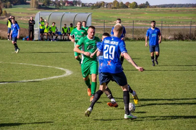 Krakow Dragoons FC and Victoria Smroków players disputing a ball in the centre of the park with the Dragoons bench in the background
