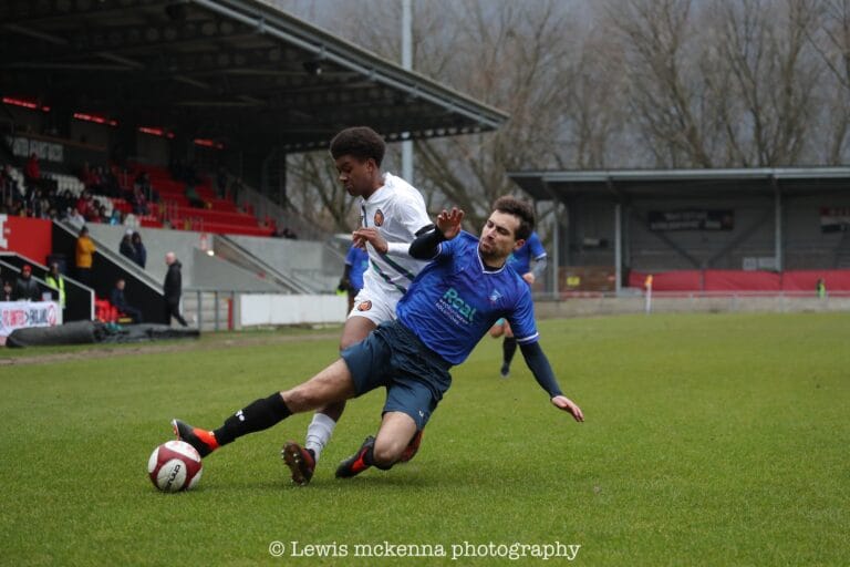 Simon Calabrese of Krakow Dragoons FC slide tackling a ball against a FC United of Manchester opponent