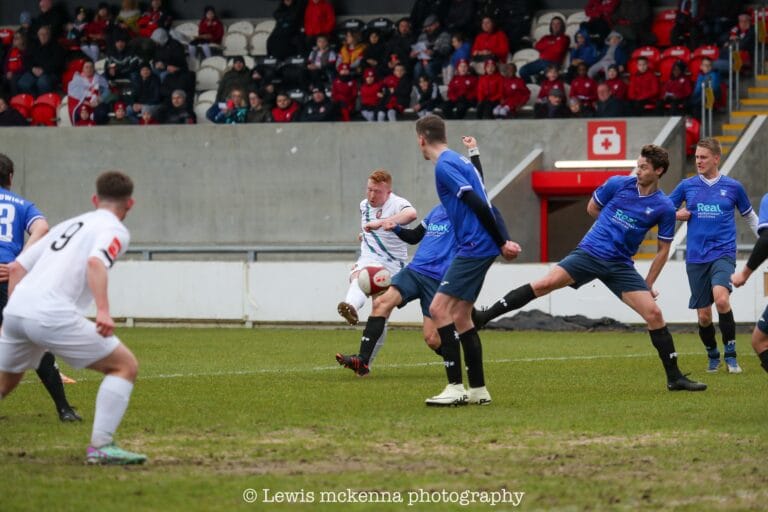 A FC United of Manchester player fires a curling shot at goal amid the Krakow Dragoons FC defenders