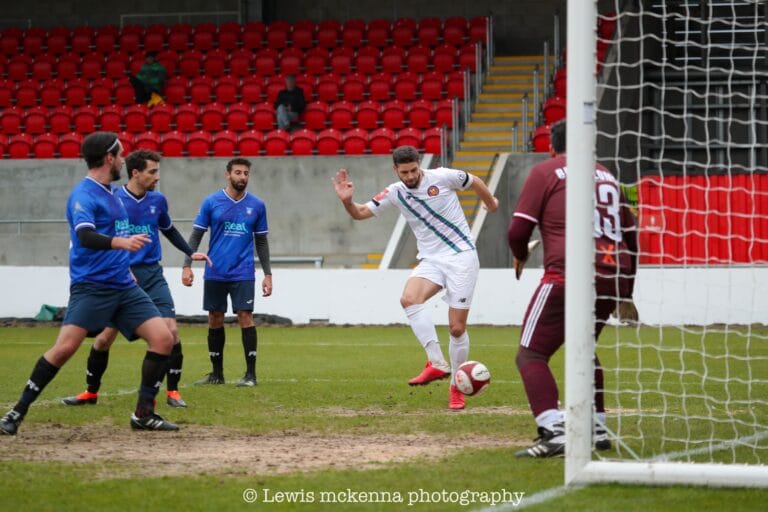 A FC United of Manchester player taps the ball into the net amid Krakow Dragoons FC players