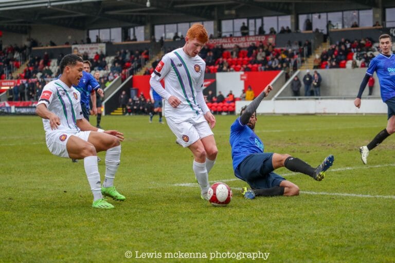 A FC United of Manchester player tries dribbling past a Krakow Dragoons FC sliding defender