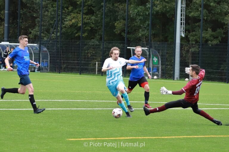 A Błękitni II Modlnica player runs past goalkeeper Marcin Obyrtacz of Krakow Dragoons FC to score a goal