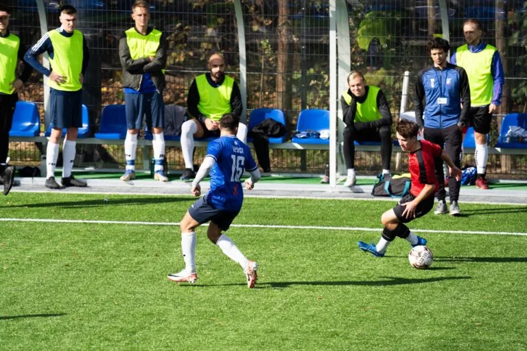 Krakow Dragoons FC players and coaches watch by the sideline as a Sportowiec Modlniczka player tries to dribble past Francesco Leuci